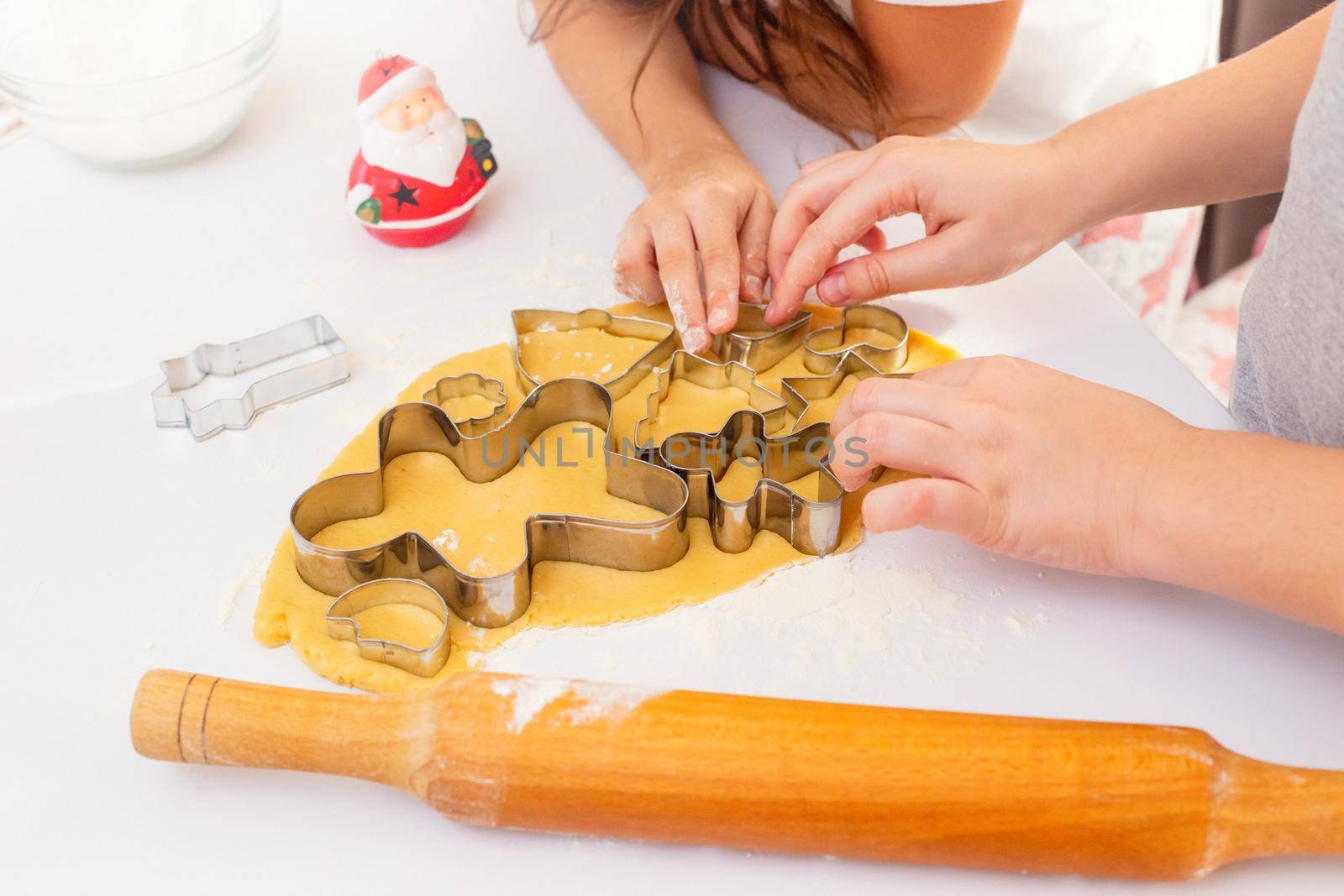 Children's hands, close-up, on a white table, cut out from the dough Christmas figured cookies in the metal form of a man, a Christmas tree and other figures. Top view