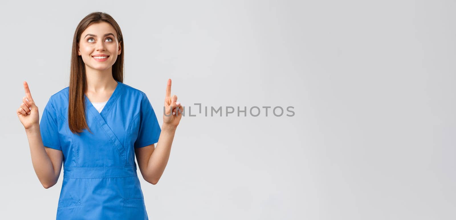 Healthcare workers, prevent virus, covid-19 test screening, medicine concept. Attractive female nurse or doctor in blue scrubs, pointing fingers and looking up with pleased smile, reading banner by Benzoix