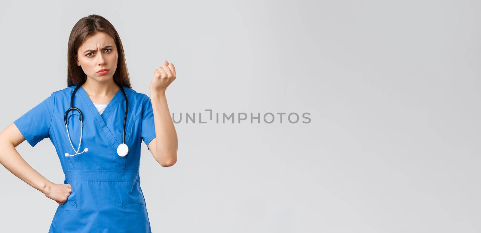 Medical workers, healthcare, covid-19 and vaccination concept. Angry and grumpy young female nurse, doctor scolding young patient breaking quarantine rules, shaking fist in threat.