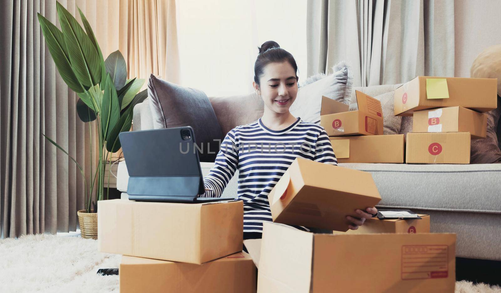 Online Marketing, Young start up small business owner writing address on cardboard box from list order. small business entrepreneur SME or freelance asian woman working with box at home by wichayada