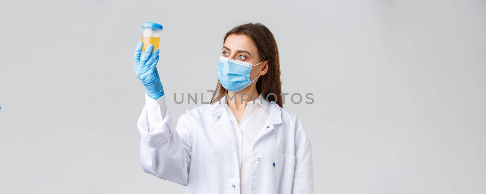 Covid-19, medical research, diagnosis, healthcare workers concept. Professional doctor in clinic lab, scrubs and medical mask, looking at urine sample, patient test on coronavirus infection.