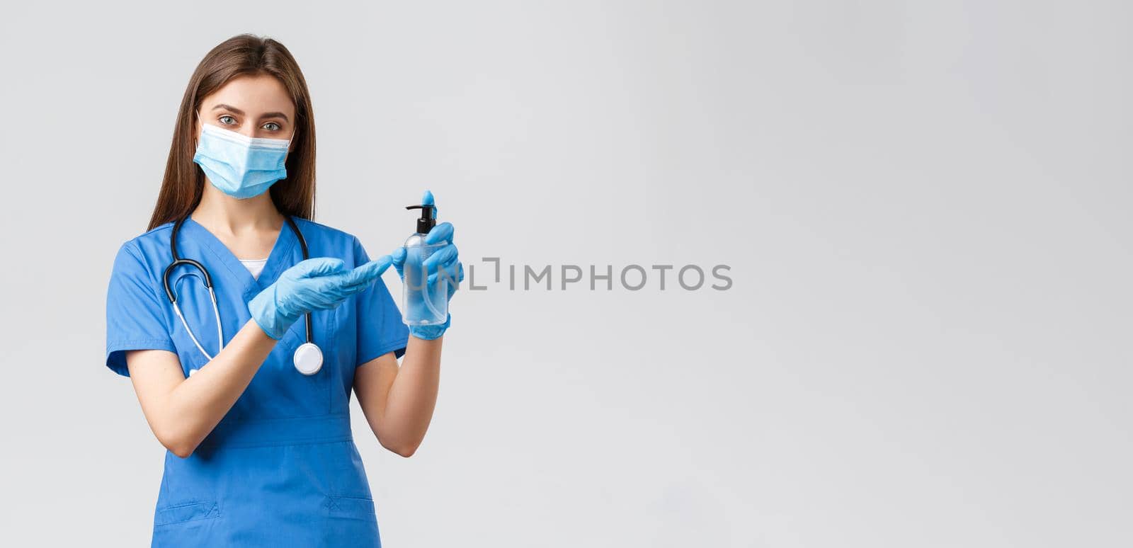 Covid-19, preventing virus, healthcare workers and quarantine concept. Pretty female nurse or doctor in blue scrubs, gloves and medical mask applying hand sanitizer to protect from coronavirus.