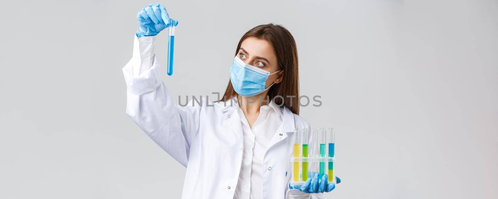 Covid-19, preventing virus, healthcare workers and quarantine concept. Doctor or nurse in clinic lab wear medical mask and gloves, looking at test-tube with coronavirus test vaccine, researching by Benzoix