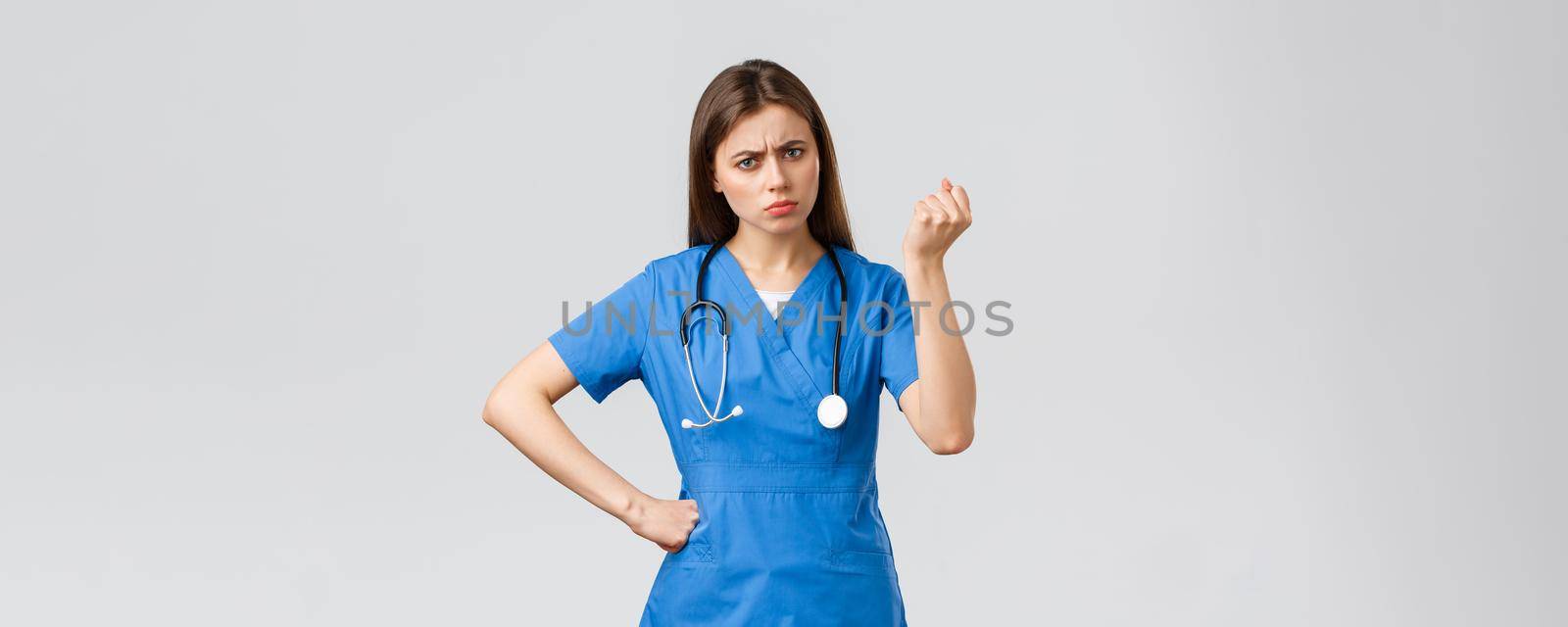 Medical workers, healthcare, covid-19 and vaccination concept. Angry and grumpy young female nurse, doctor scolding young patient breaking quarantine rules, shaking fist in threat.