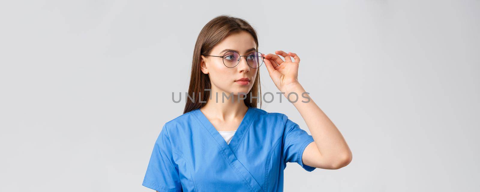 Healthcare workers, medicine, insurance and covid-19 pandemic concept. Professional young smart doctor or nurse, female intern in scrubs and glasses, looking right at banner serious face.