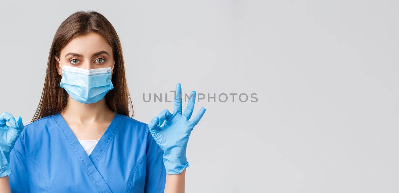 Covid-19, preventing virus, health, healthcare workers and quarantine concept. Professional female nurse or doctor in clinic, blue scrubs and medical mask, show okay sign, all under control.