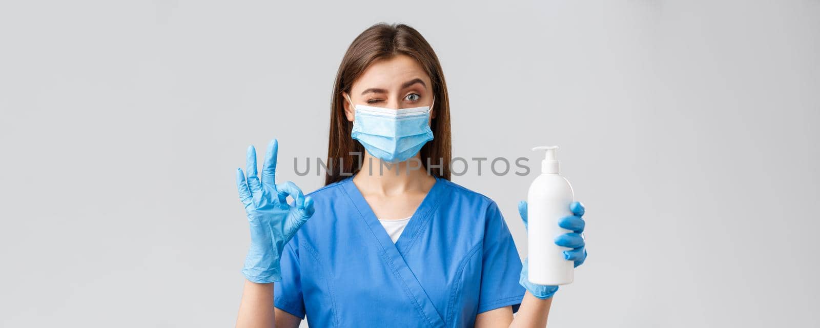 Covid-19, preventing virus, healthcare workers and quarantine concept. Confident cute female nurse or doctor in blue scrubs, medical mask and gloves, approve and recommend soap or hand sanitizer by Benzoix