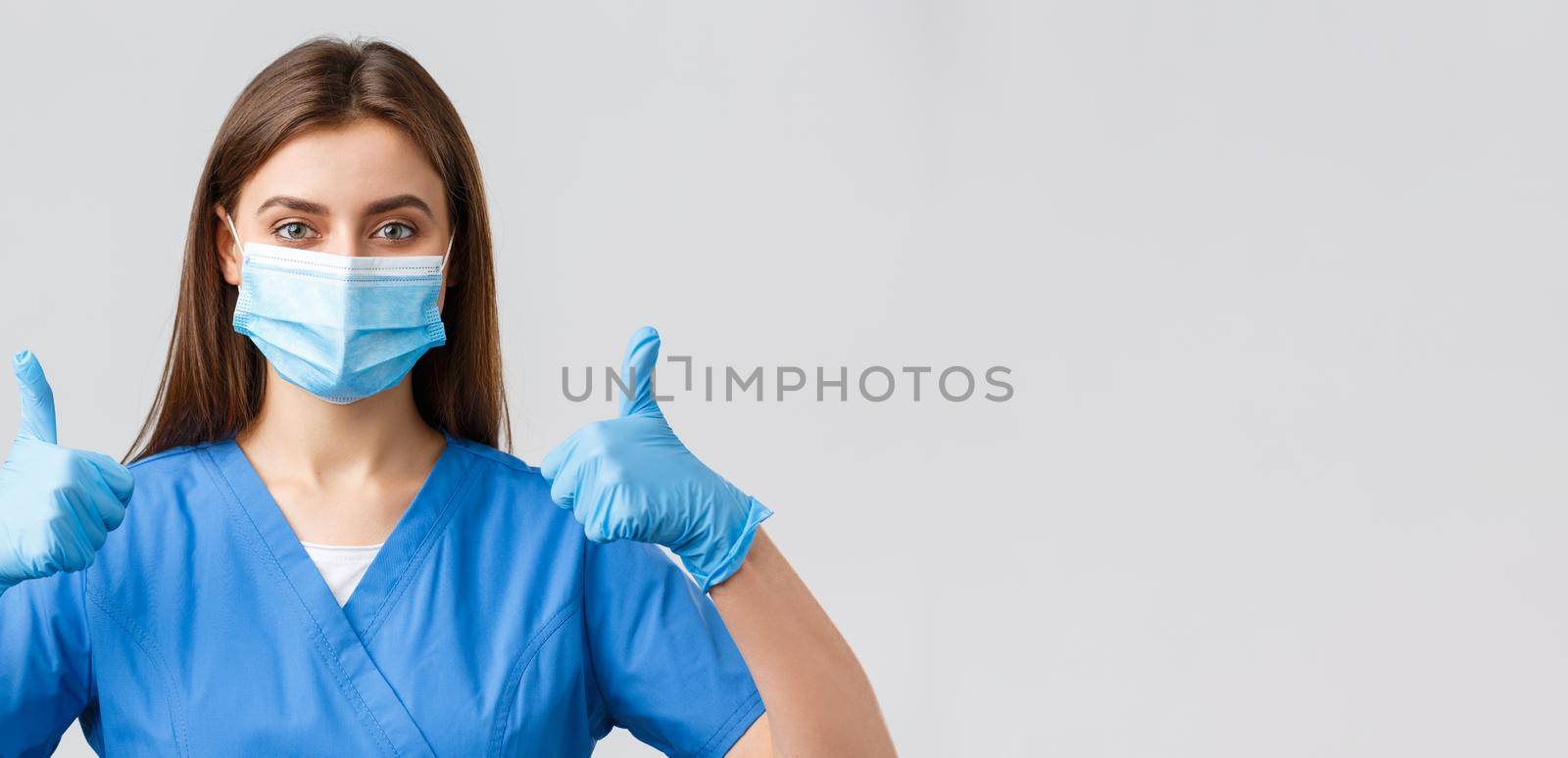 Covid-19, preventing virus, health, healthcare workers and quarantine concept. Close-up of supportive female nurse or doctor in blue scrubs, medical mask and gloves, thumbs-up in approval.