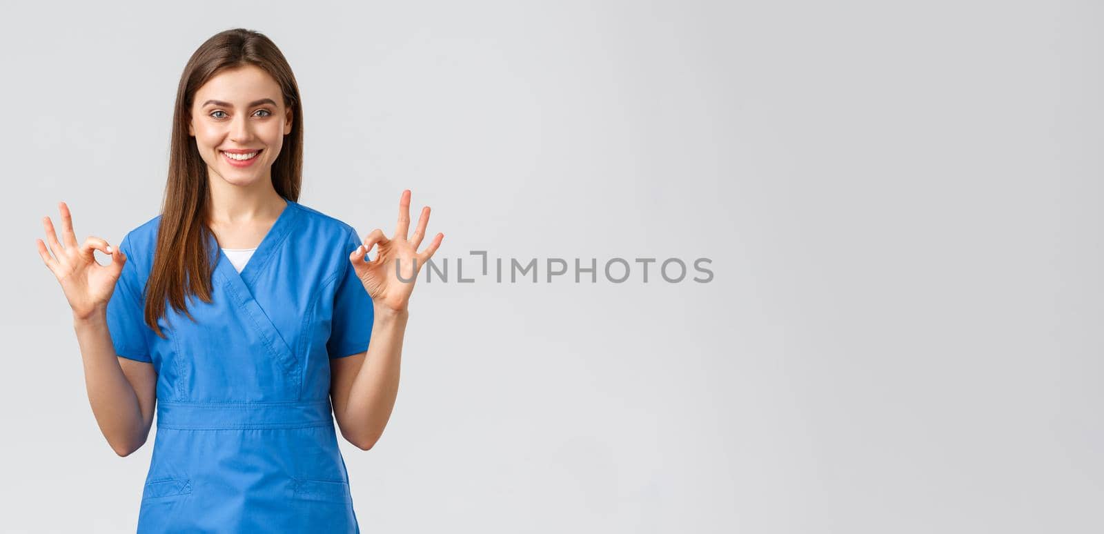 Healthcare workers, prevent virus, insurance and medicine concept. Confident young female nurse, doctor in blue scrubs assure quality of test results in their clinic lub, show okay sign, guarantee.