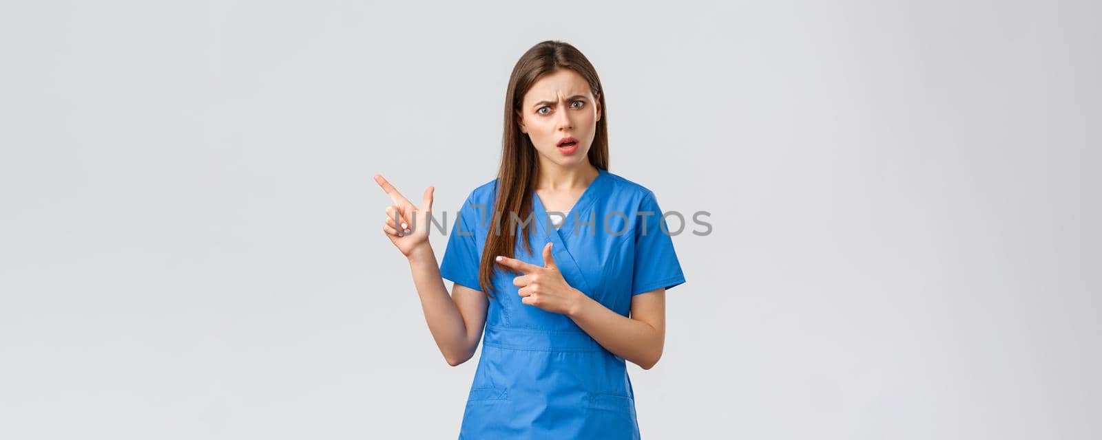 Healthcare workers, prevent virus, insurance and medicine concept. Concerned and puzzled nurse or doctor look confused, pointing fingers left, need answer, asking question, grey background.