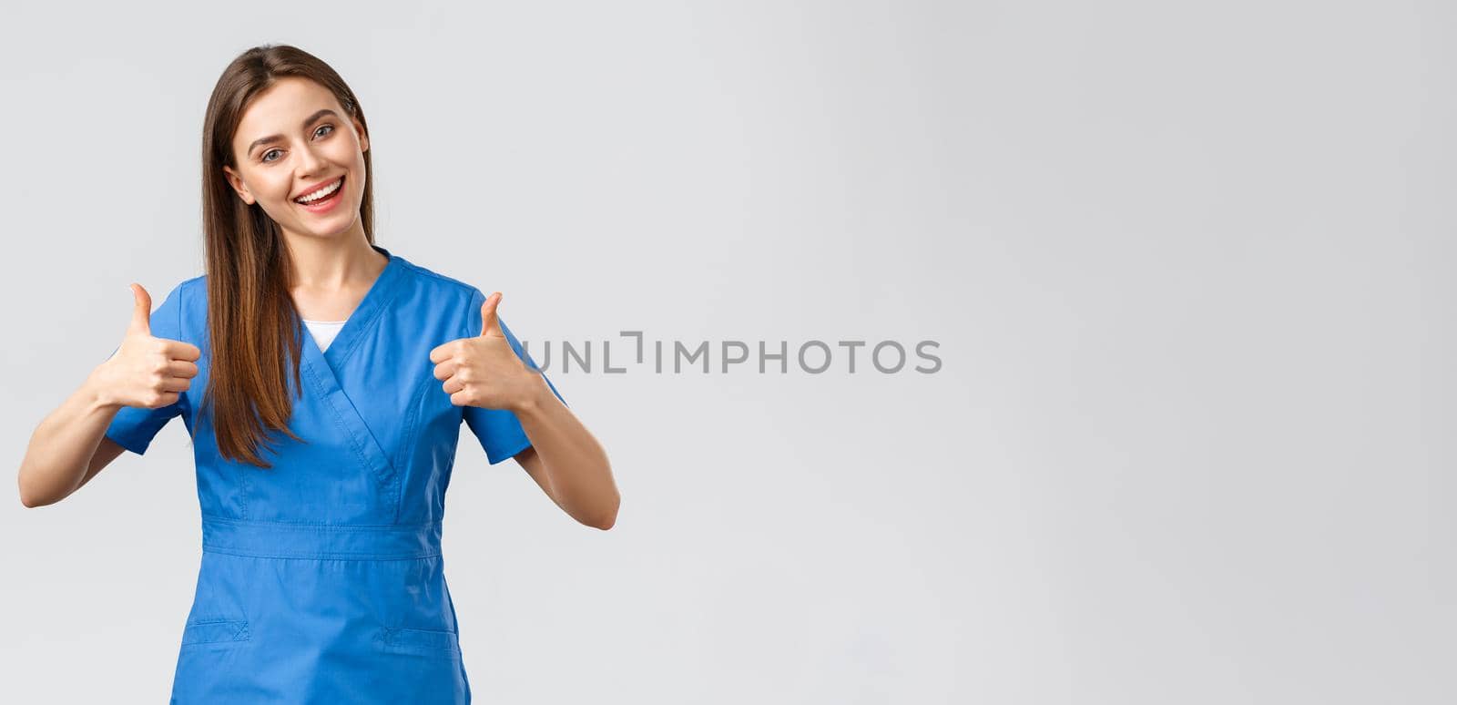 Healthcare workers, prevent virus, insurance and medicine concept. Optimistic and enthusiastic female nurse, doctor in blue scrubs, thumbs-up and smiling, encourage patients stay home.