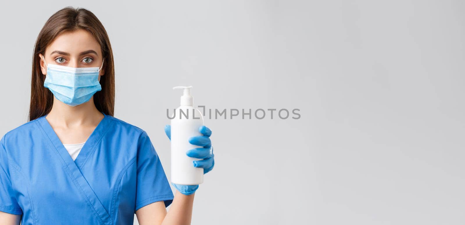 Covid-19, preventing virus, health, healthcare workers and quarantine concept. Serious-looking medical worker, nurse or doctor in blue scrubs and medical mask, showing hand sanitizer or soap by Benzoix