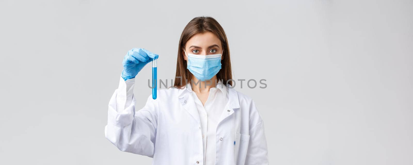 Covid-19, preventing virus, healthcare workers and quarantine concept. Determined female doctor or nurse in medical mask and scrubs, showing test-tube with coronavirus vaccine by Benzoix