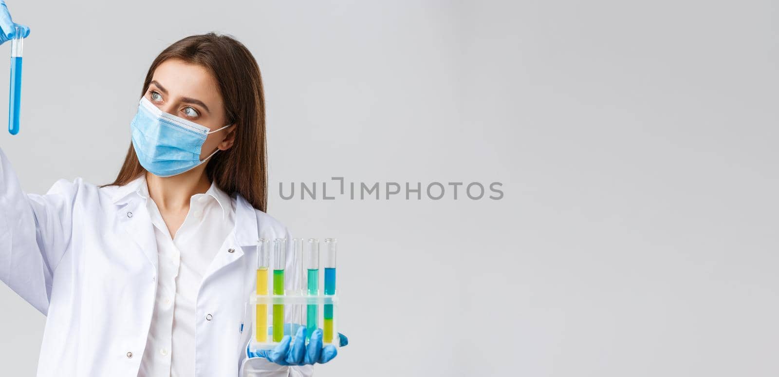 Covid-19, preventing virus, healthcare workers and quarantine concept. Doctor or nurse in clinic lab wear medical mask and gloves, looking at test-tube with coronavirus test vaccine, researching by Benzoix