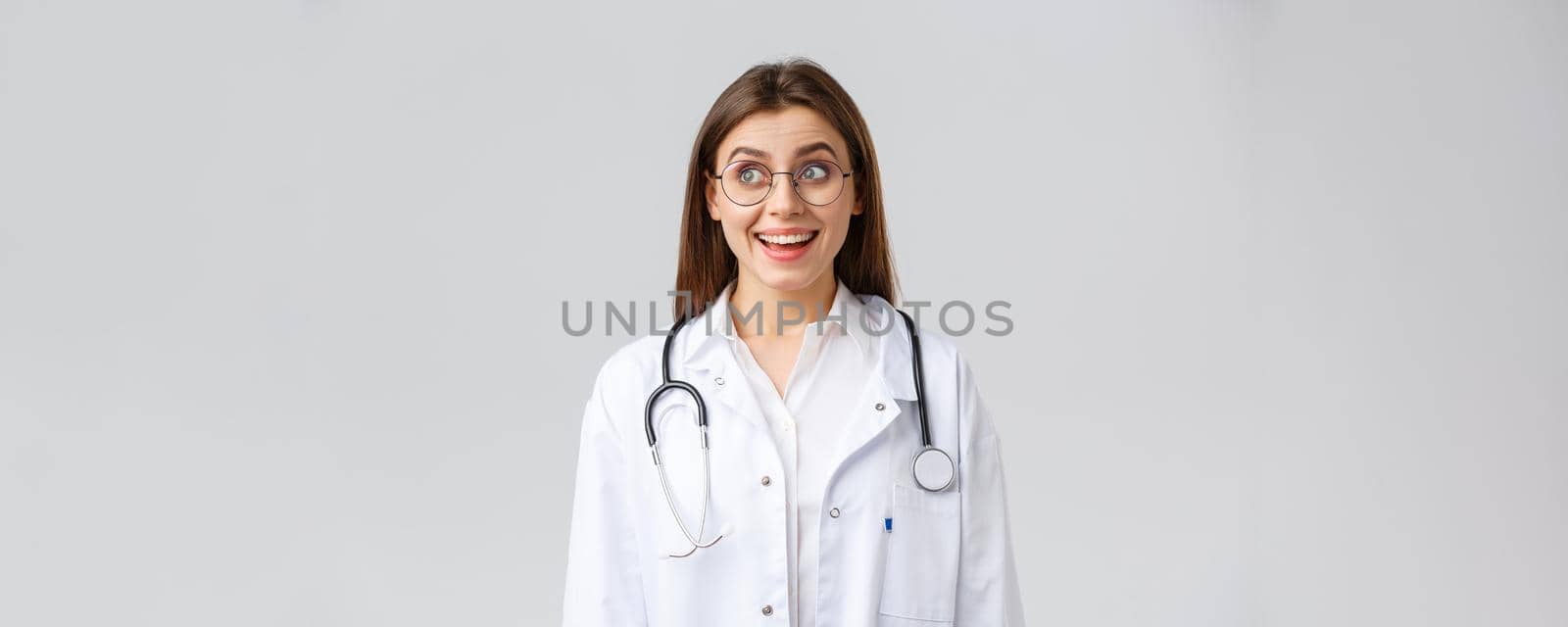 Healthcare workers, medicine, insurance and covid-19 pandemic concept. Happy optimistic female doctor, physician with stethoscope in white scrubs and glasses, look upper left corner with upbeat smile by Benzoix