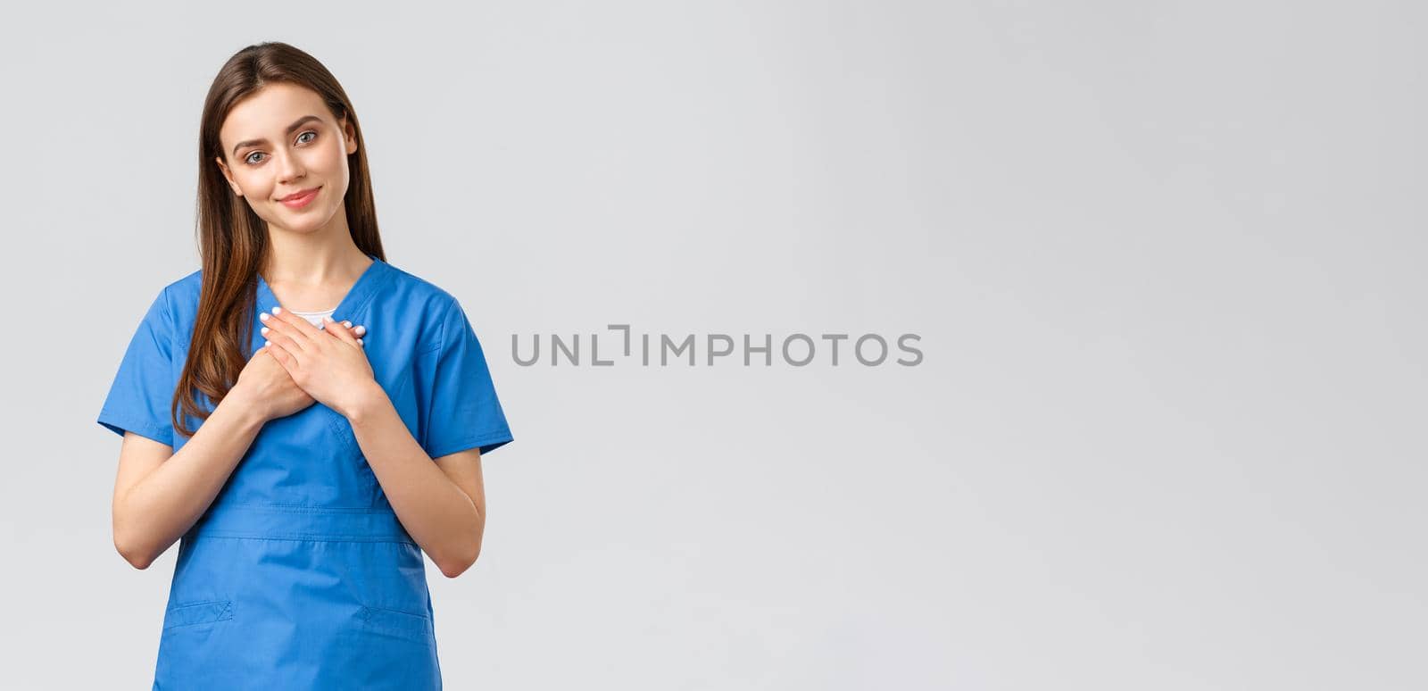 Healthcare workers, prevent virus, insurance and medicine concept. Touched and flattered female nurse or doctor in blue scrubs, tilt head and touch heart, smile from compliment, nice gesture.