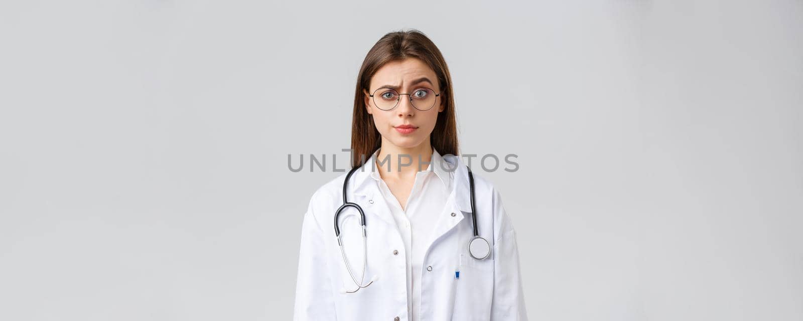 Healthcare workers, medicine, insurance and covid-19 pandemic concept. Skeptical and confused female doctor in white scrubs, medical suit and glasses, raise eyebrow judgemental, smirk displeased.