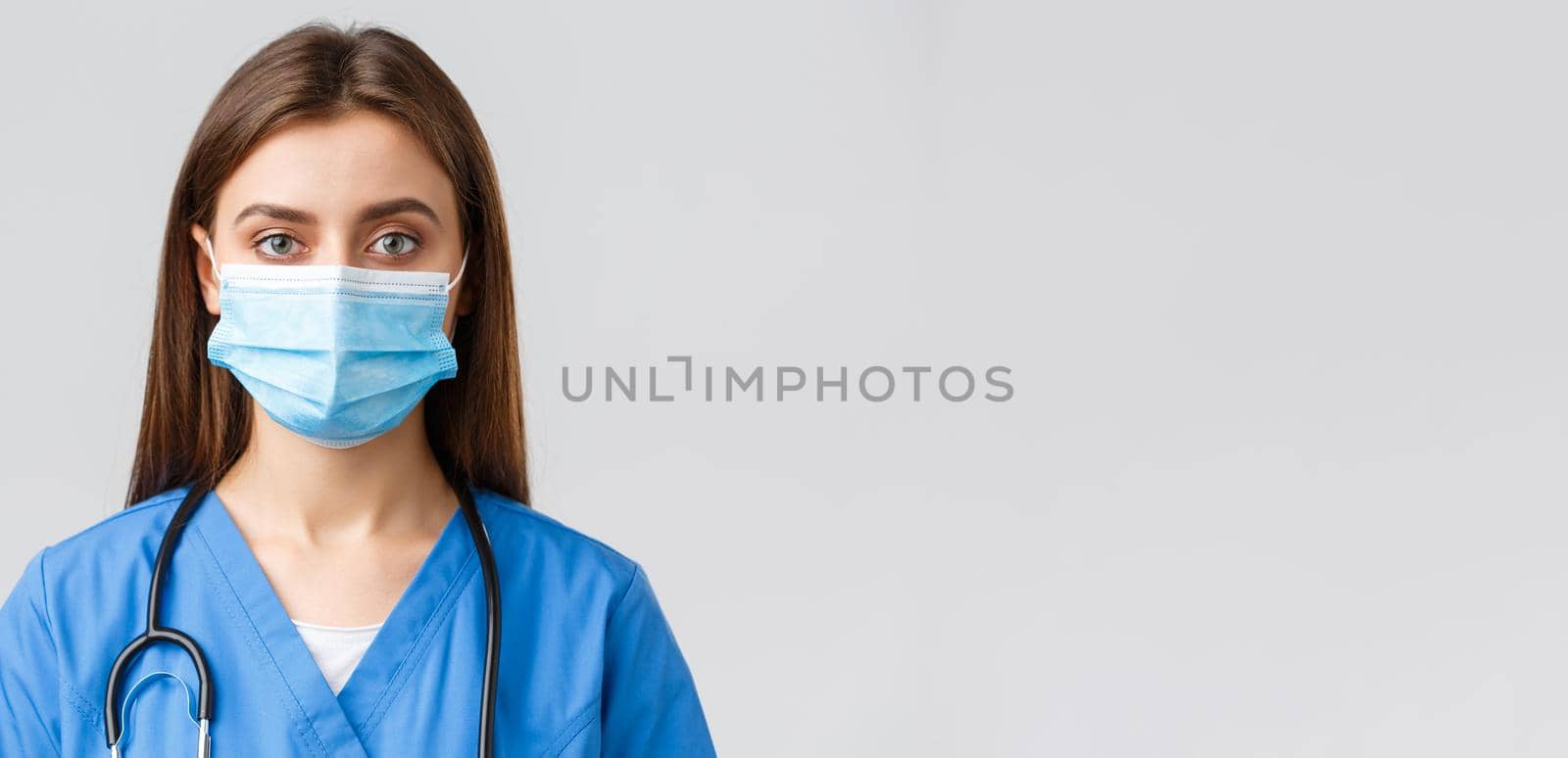 Covid-19, preventing virus, health, healthcare workers and quarantine concept. Close-up young female nurse or doctor in blue scrubs and medical mask looking serious at camera.