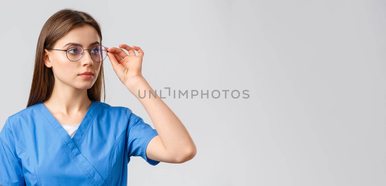 Healthcare workers, medicine, insurance and covid-19 pandemic concept. Professional young smart doctor or nurse, female intern in scrubs and glasses, looking right at banner serious face.