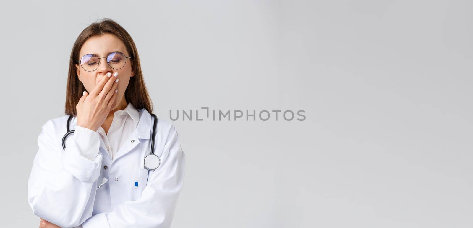 Healthcare workers, medicine, insurance and covid-19 pandemic concept. Young doctor in white scrubs, female physician working hard night shift during coronavirus, yawning and cover mouth by Benzoix