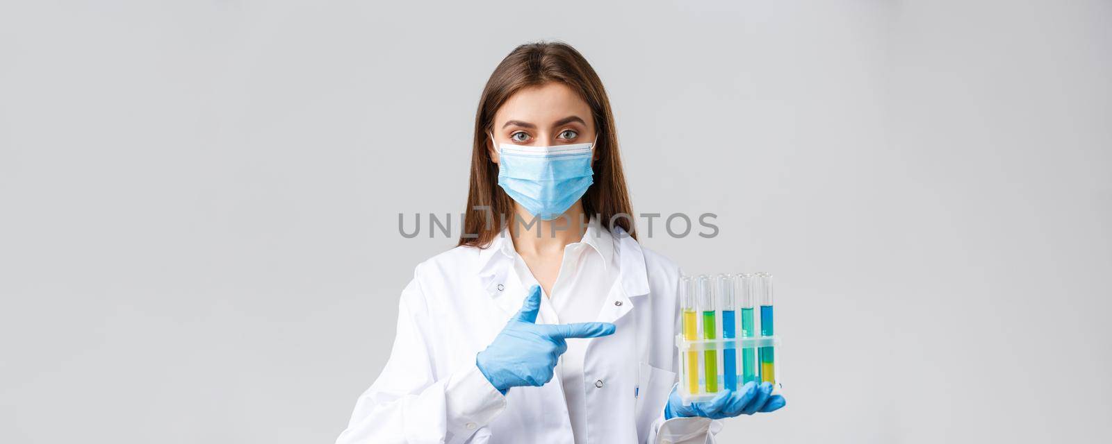 Covid-19, preventing virus, healthcare workers concept. Professional doctor in personal protective equipment, medical mask, pointing at test-tube with coronavirus vaccine, patient samples.