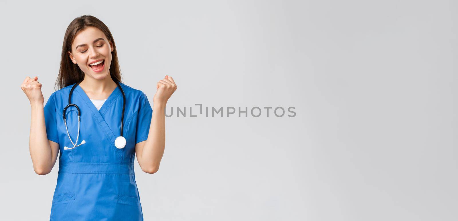 Medical workers, healthcare, covid-19 and vaccination concept. Happy cheerful female nurse, pretty enthusiastic doctor in blue scrubs, passed test, fist pump in rejoice, smiling relieved.