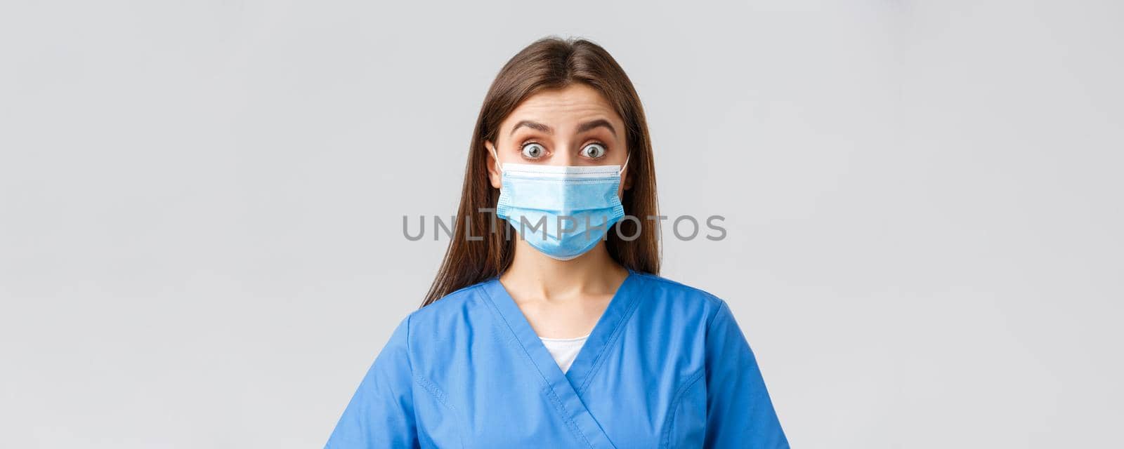 Covid-19, preventing virus, health, healthcare workers and quarantine concept. Surprised female nurse or doctor in blue scrubs and medical mask, staring shocked and excited at camera by Benzoix