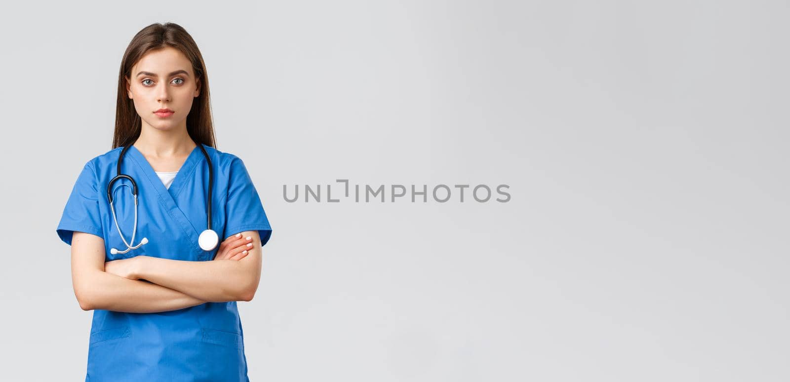 Medical workers, healthcare, covid-19 and vaccination concept. Serious and determined professional female nurse, doctor in blue scrubs with stethoscope, cross arms chest and look camera ready.