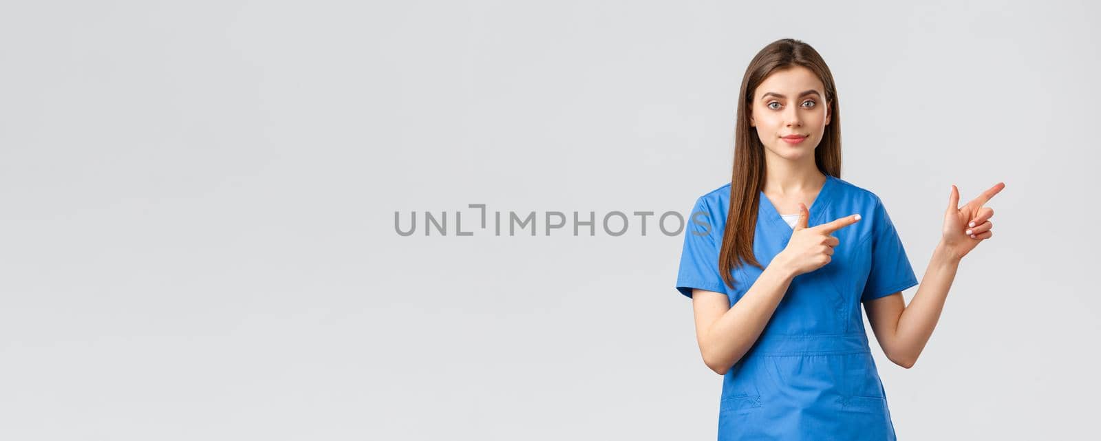 Healthcare workers, prevent virus, insurance and medicine concept. Young nurse or doctor in blue scrubs pointing fingers right, recommend banner or promo for clinic patients.