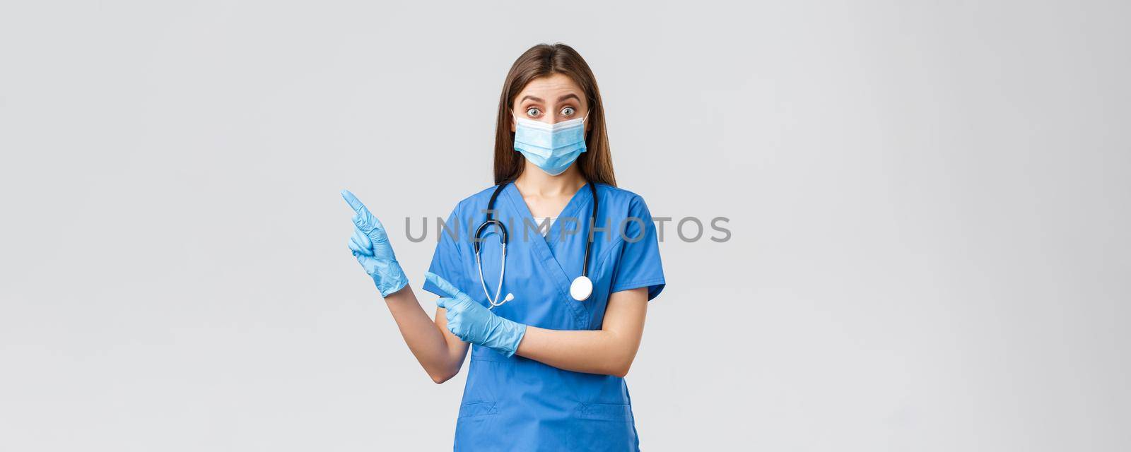 Covid-19, preventing virus, health, healthcare workers and quarantine concept. Interested and questioned female doctor, nurse in blue scrubs and medical mask, asking question pointing left by Benzoix