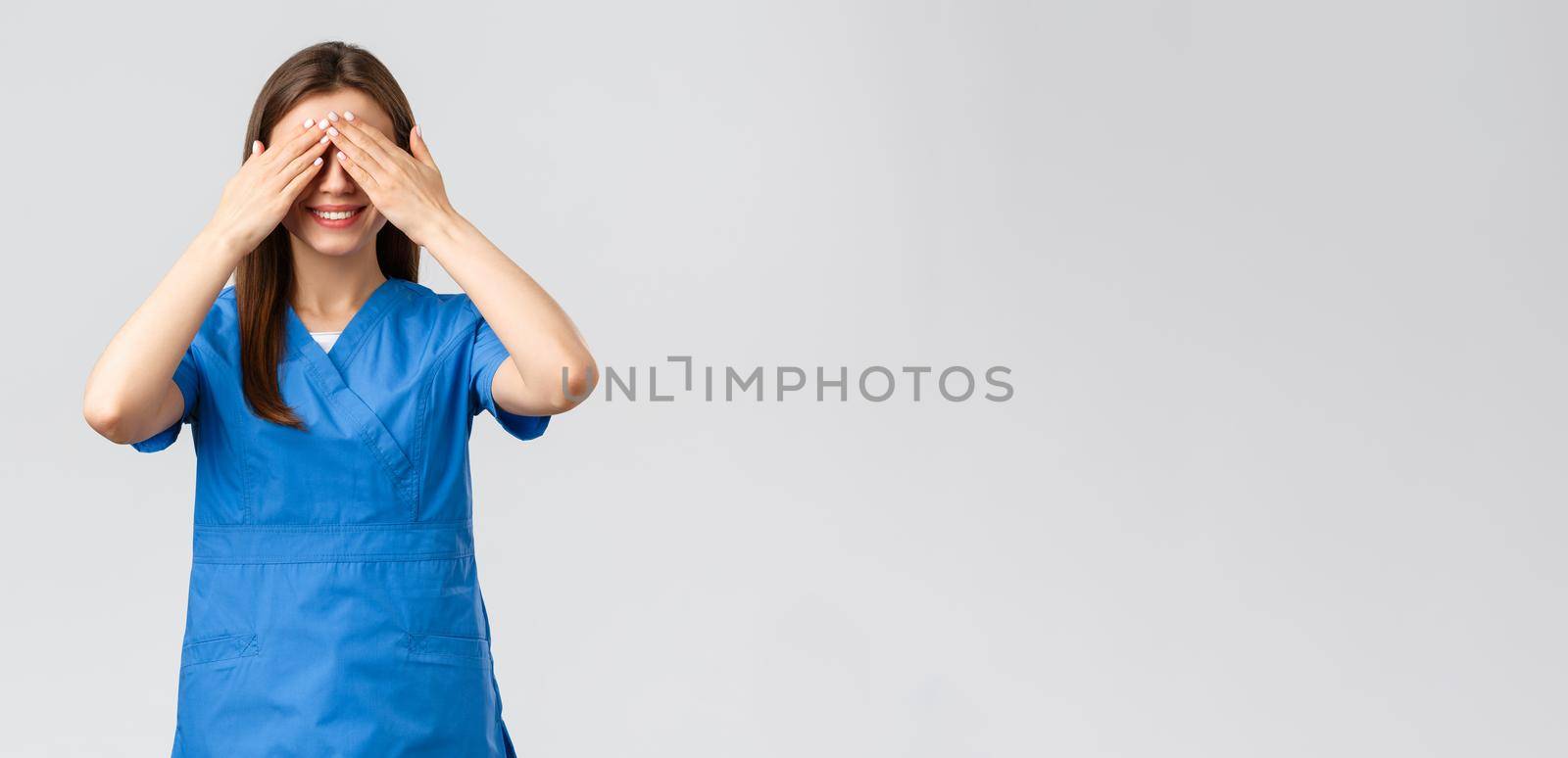 Healthcare workers, prevent virus, insurance and medicine concept. Young optimistic female nurse, doctor in scrubs, shut eyes with hands and smiling, anticipating surprise, being blindfolded by Benzoix