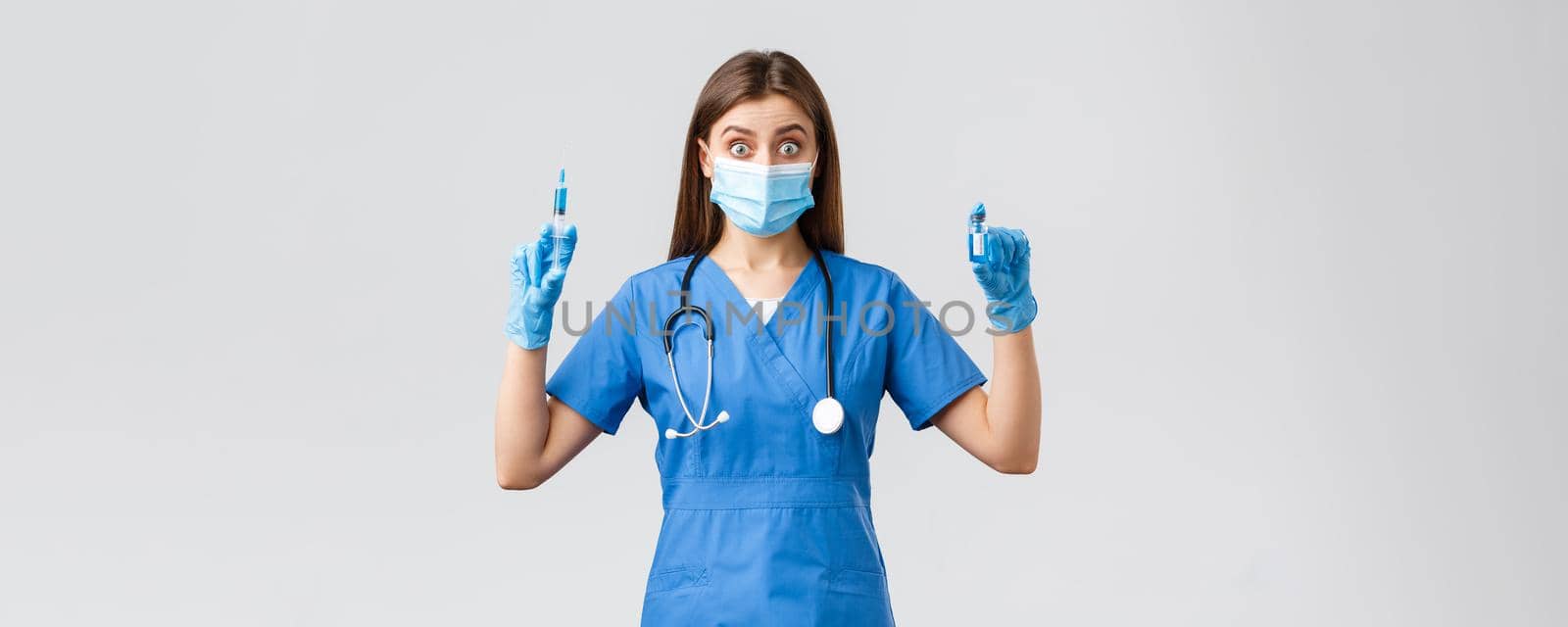 Covid-19, preventing virus, health, healthcare workers and quarantine concept. Excited female nurse in blue scrubs, doctor in clinic holding syringe and ampoule with coronavirus vaccine by Benzoix