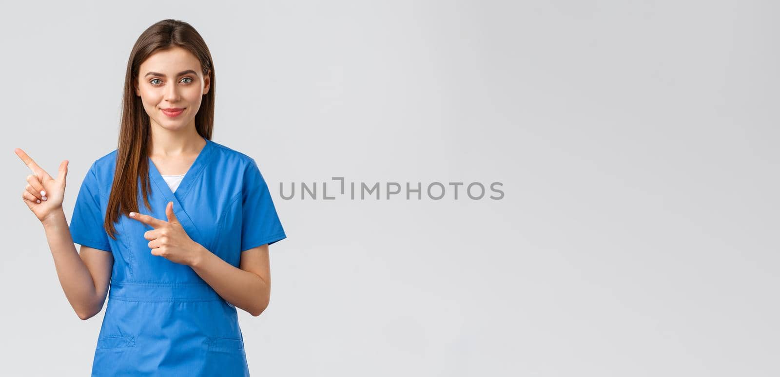 Healthcare workers, prevent virus, insurance and medicine concept. Smiling attractive female doctor or nurse in blue scrubs pointing fingers left to show patients advertisement, important info by Benzoix