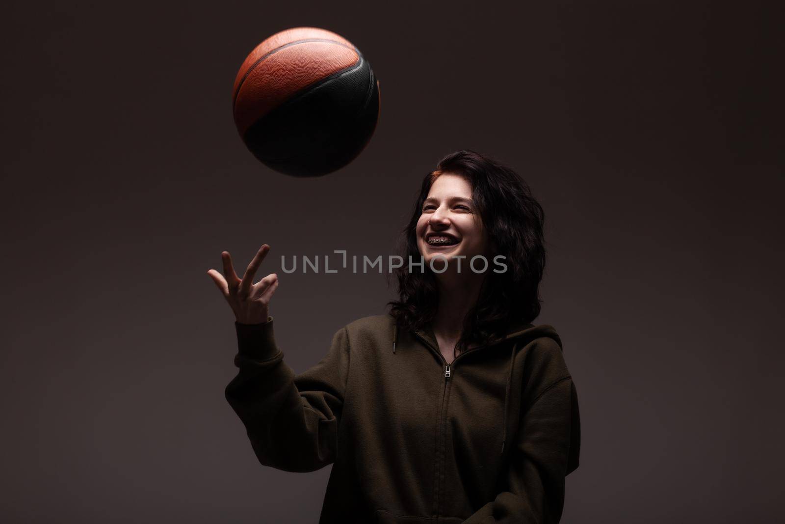 Teenage girl with dental braces holding basketball. Studio portrait on dark background.. by kokimk