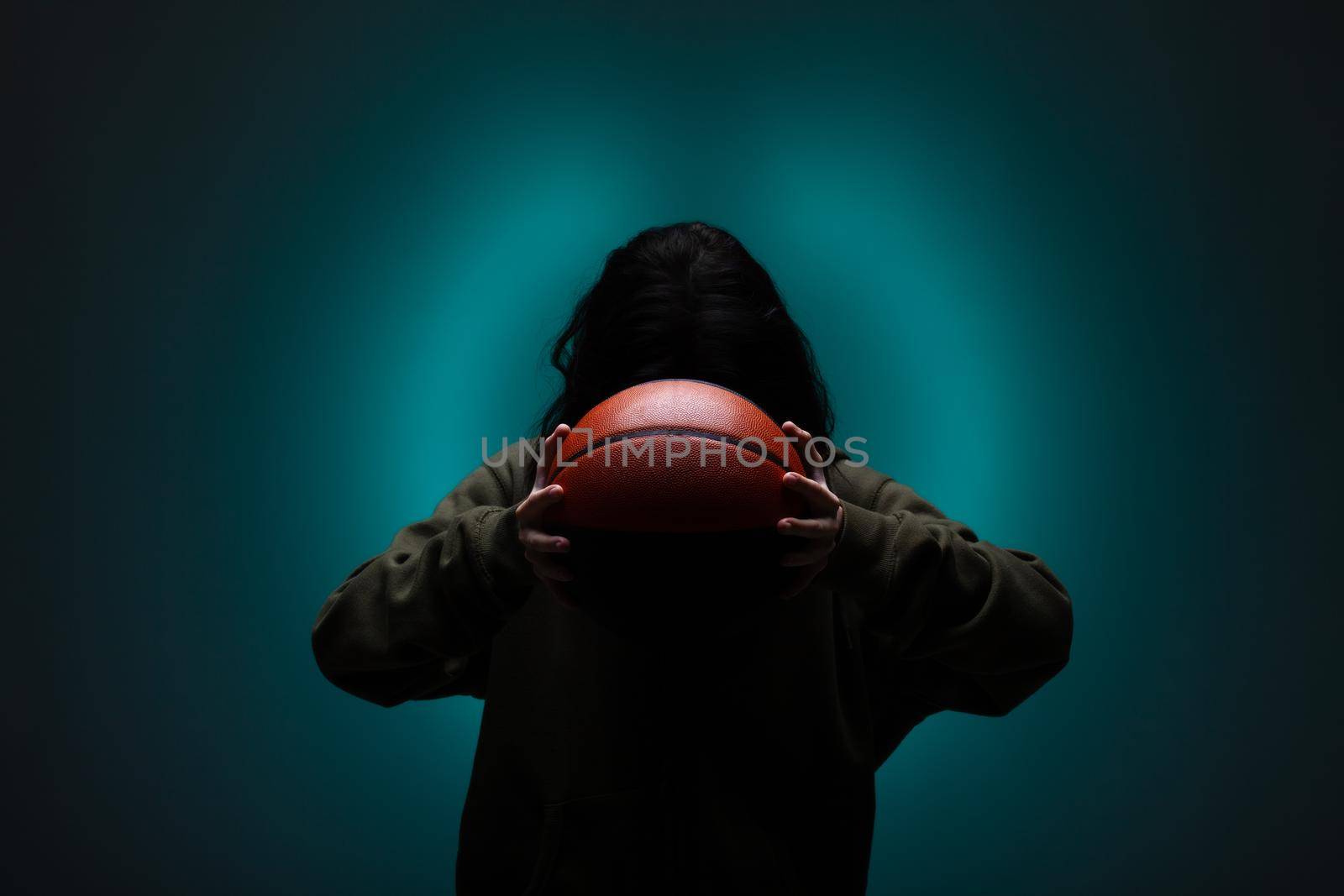 Teenage girl with basketball. Silhouette studio portrait with neon blue colored background.