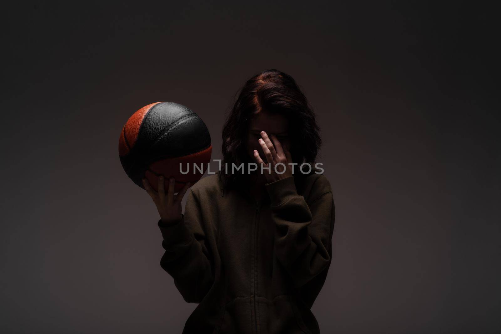 Teenage girl with basketball. Silhouette studio portrait on dark background.