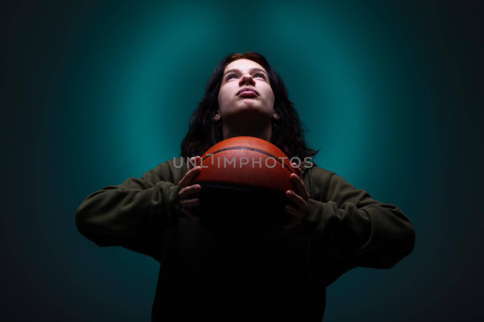 Teenage girl with basketball. Studio portrait with neon blue colored background.