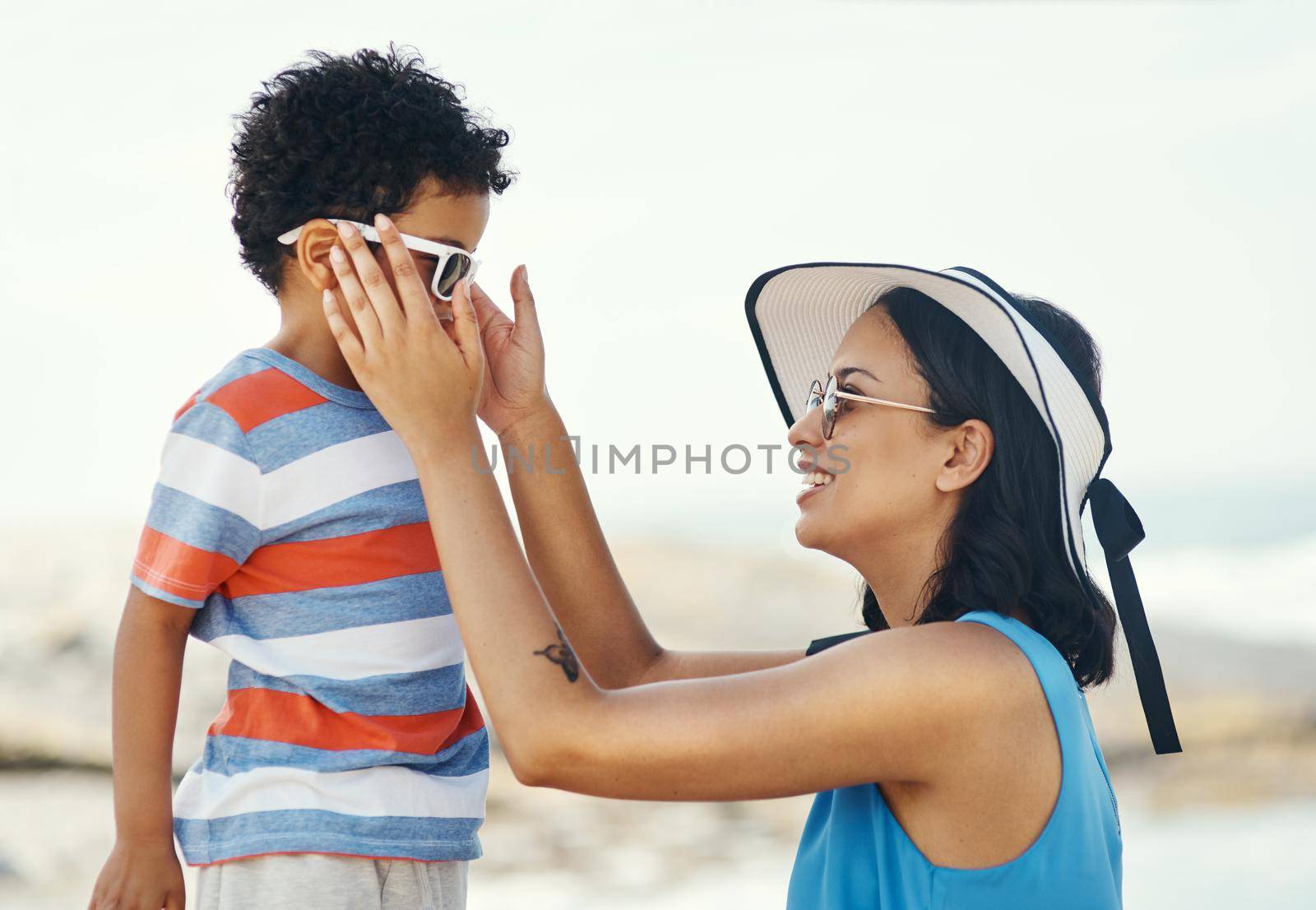 Sunglasses are really helpful for protecting your eyes. Shot of a mother applying sunscreen to her son at the beach. by YuriArcurs