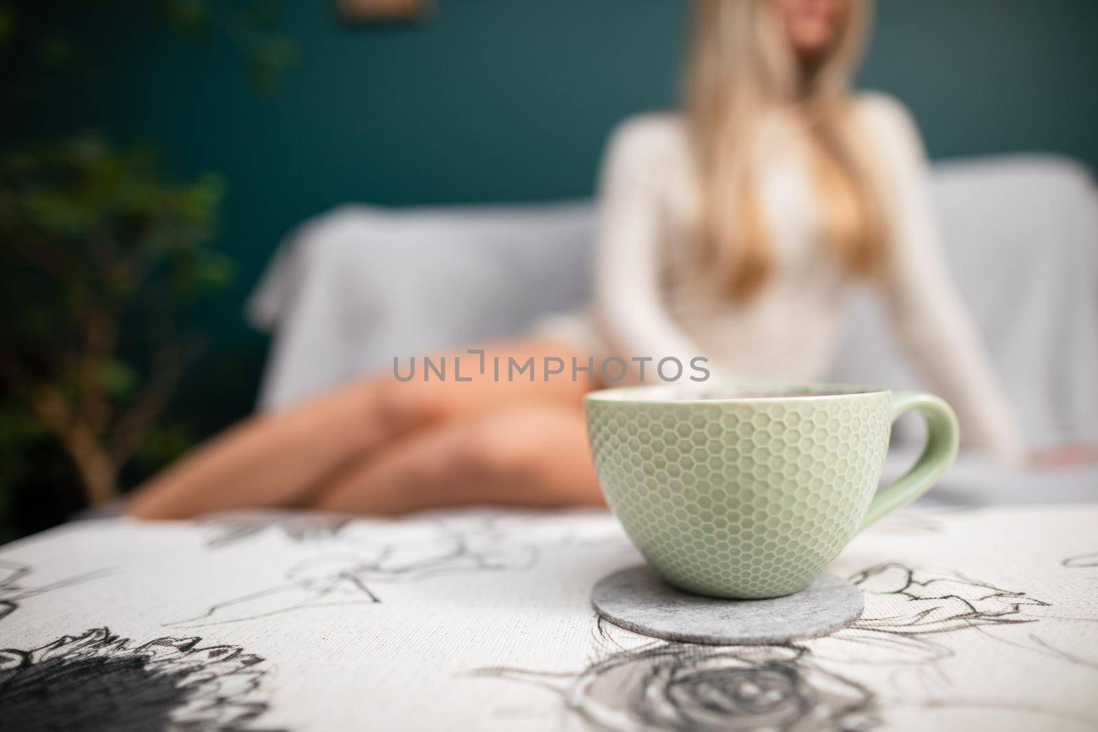 A young sexy woman with shapely legs sits on a sofa and a cup of aromatic coffee stands in front of her.