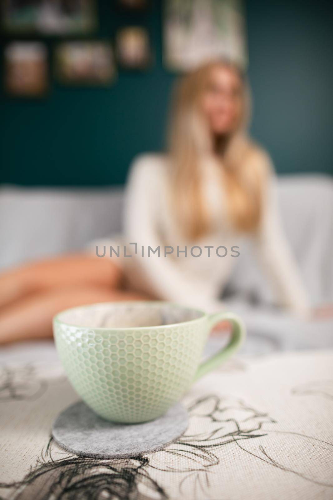 A young sexy woman with shapely legs sits on a sofa and a cup of aromatic coffee stands in front of her.