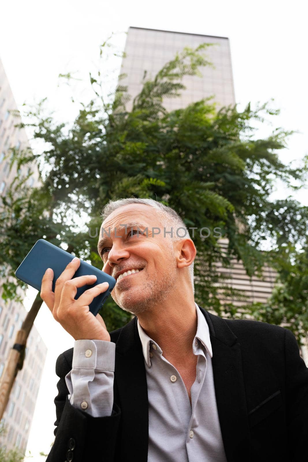 Smiling caucasian man sending voice message with mobile phone outdoors. Copy space. Vertical image. Business and technology concept.