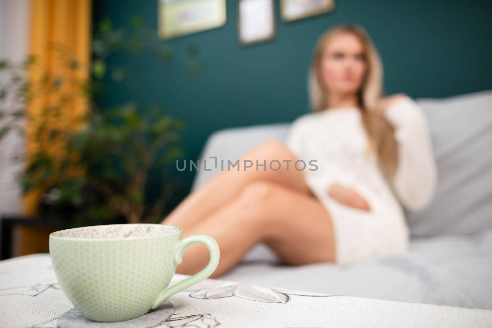 A young sexy woman with shapely legs sits on a sofa and a cup of aromatic coffee stands in front of her.