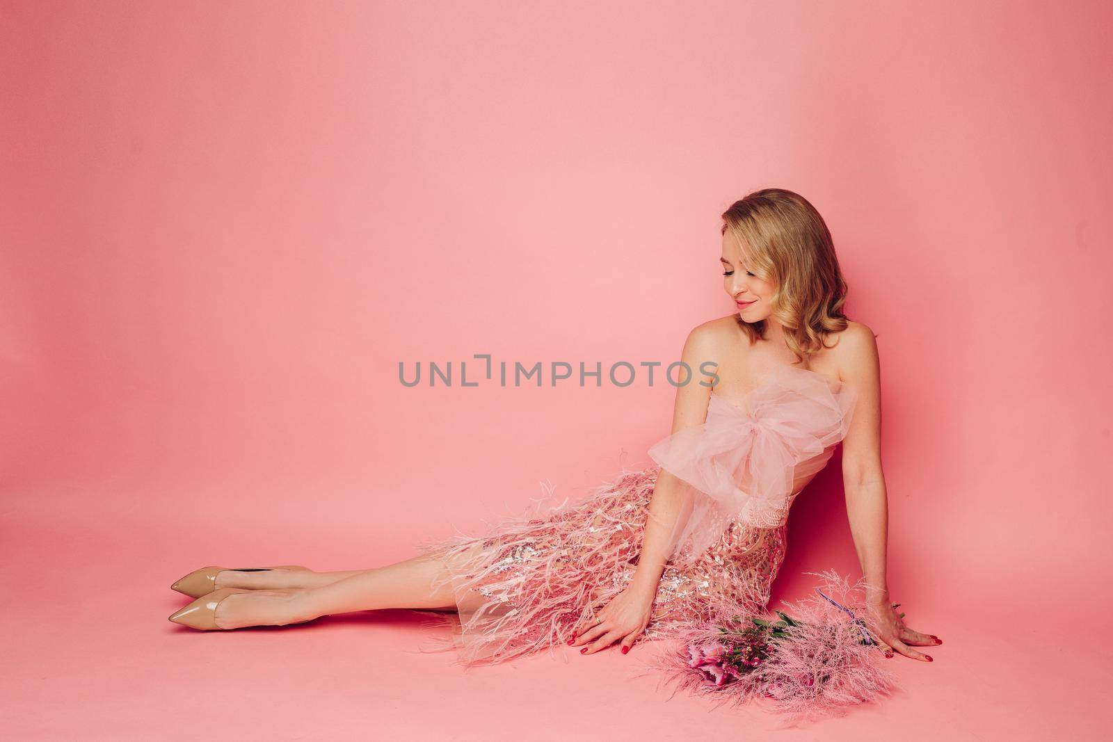 A beautiful woman is sitting with flowers on a pink background, isolated. Holiday, flowers, the concept of celebration and joy.