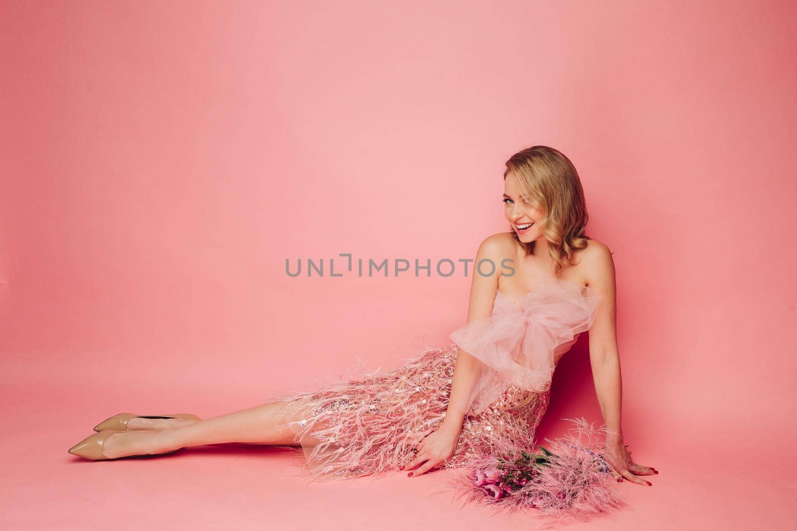 Beautiful woman sitting with flowers on pink background.