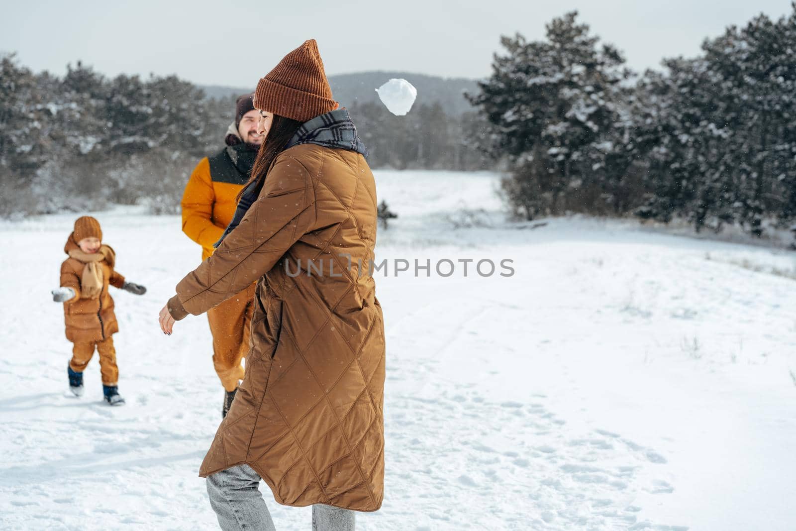 Young family having fun in winter snowy forest playing snowballs