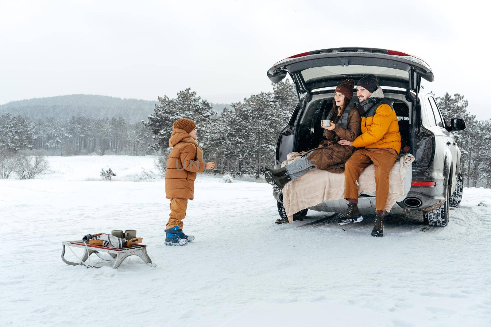 Winter portrait of a family sit on car trunk enjoy their vacation in snowy forest