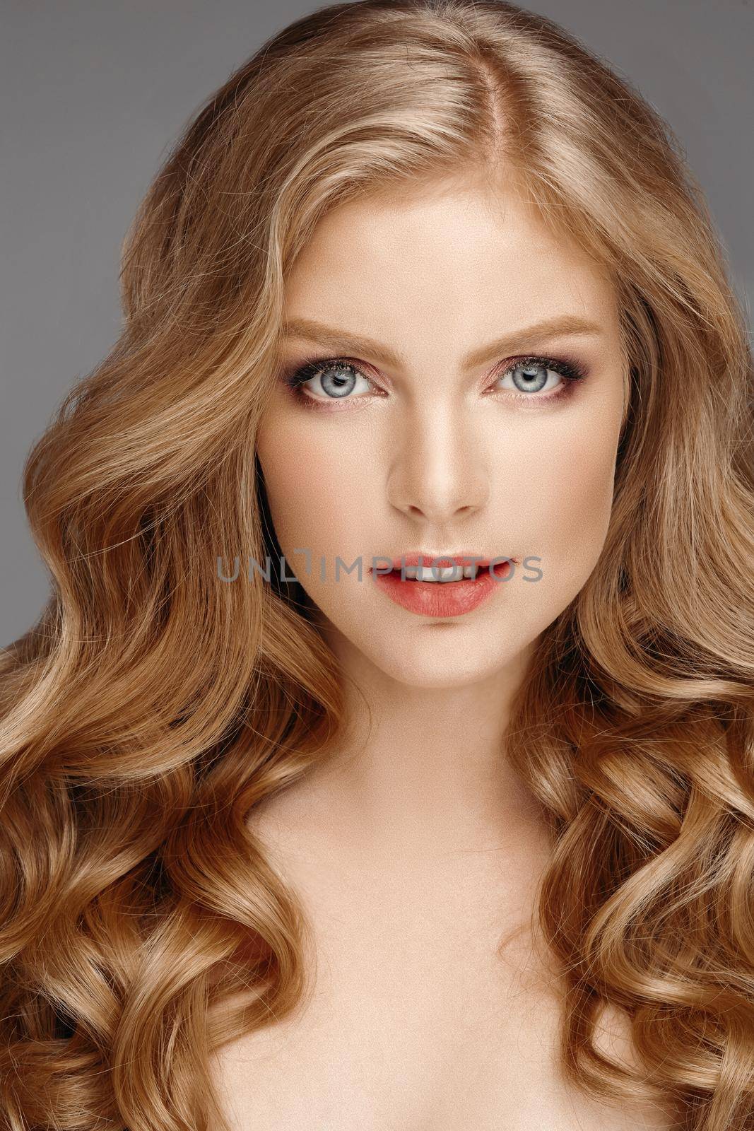 Studio fashion portrait of attractive sensual young woman with long wavy fair hair and blue eyes looking at camera. Natural beauty concept. Caucasian.