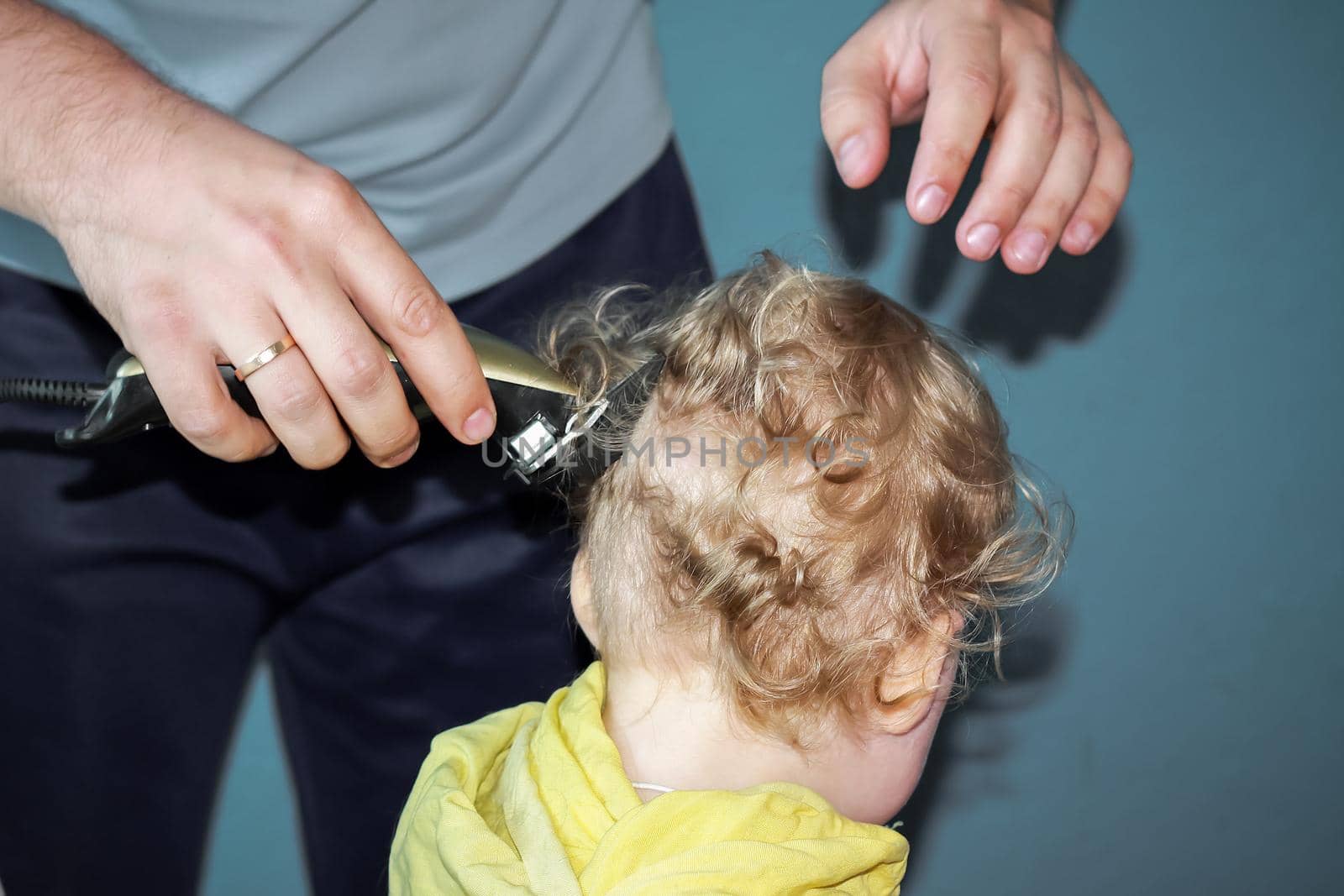 The first haircut on the head of a little boy in his life. A man is a father who cuts his son's hair. Shave the curls off the baby's head with an electric razor.