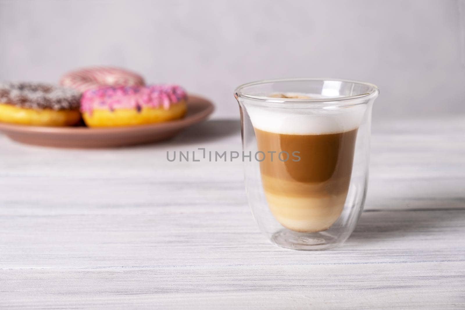 Glazed decorated donuts on plates and coffee latte or cappuccino with milk foam in a heat-resistant glass cup. Selective focus.