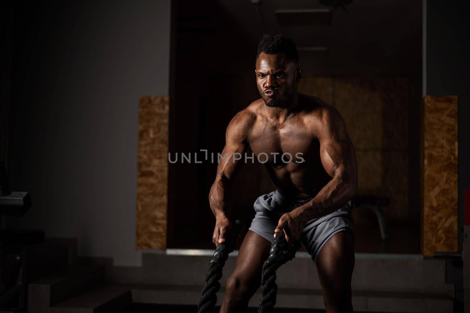 Attractive african american man with naked torso doing endurance exercises with trope. by mrwed54